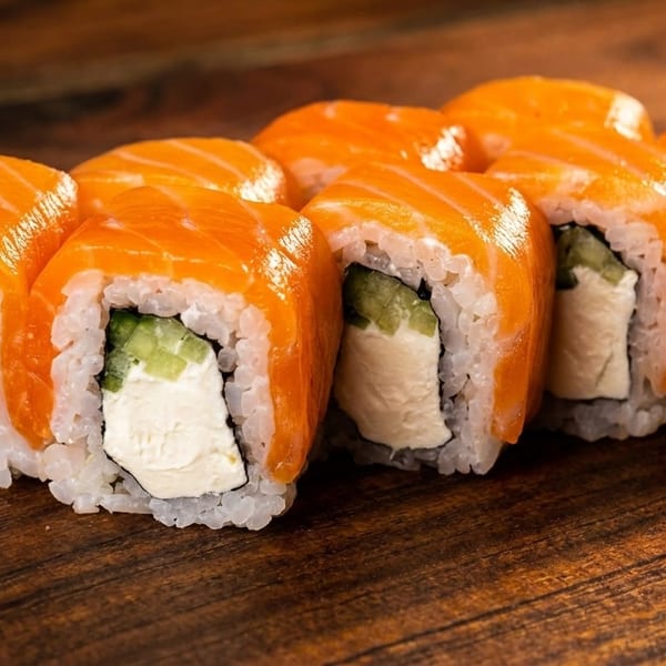 Eight salmon sushi rolls with cream cheese and cucumber on a wooden surface.
