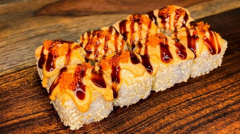 Eight sushi rolls with sesame seeds, topped with orange sauce, dark glaze, and orange roe.