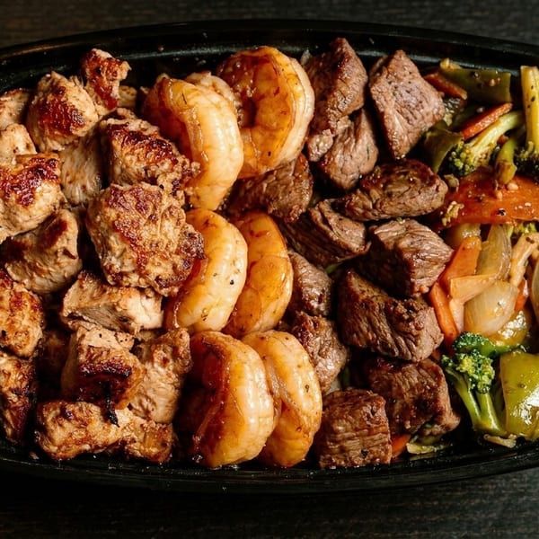 A black container filled with grilled chicken, shrimp, steak, and mixed vegetables.