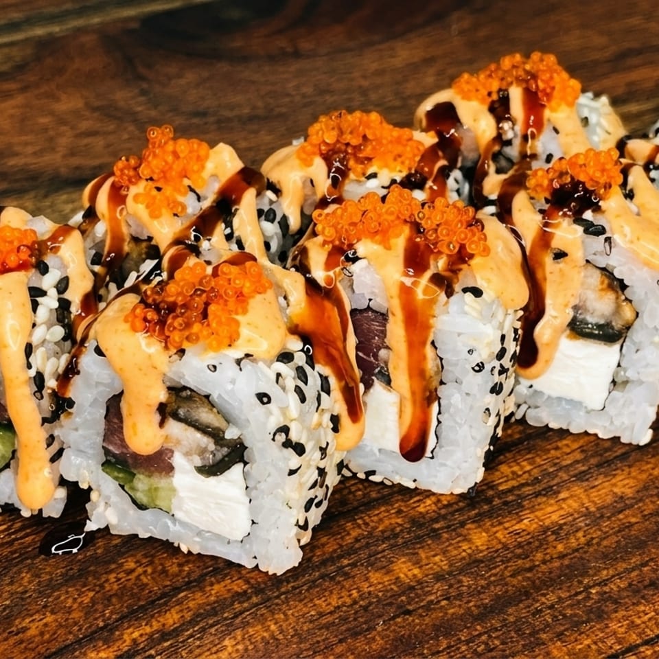 Sushi rolls with orange roe, creamy sauce, and dark drizzle on a wooden surface.