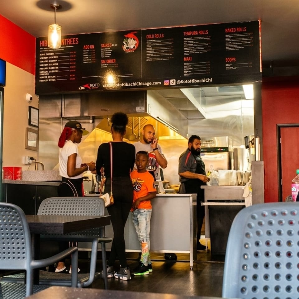Customers wait at the counter of a Koto Hibachi restaurant with a Pepsi cooler nearby.